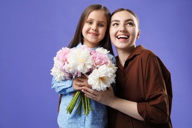 Photo of Mother and her daughter with bouquet of beautiful peonies on purple background, space for text