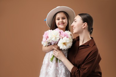 Photo of Mother and her daughter with bouquet of beautiful peonies on brown background, space for text