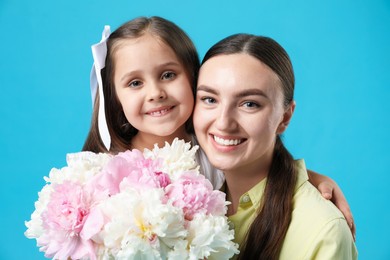 Photo of Mother and her daughter with bouquet of beautiful peonies on light blue background