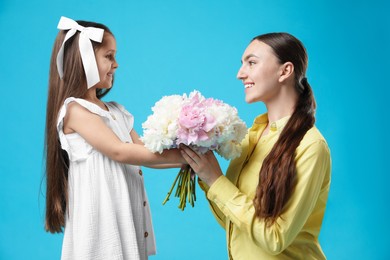 Photo of Cute little girl giving her mother bouquet of beautiful peonies on light blue background