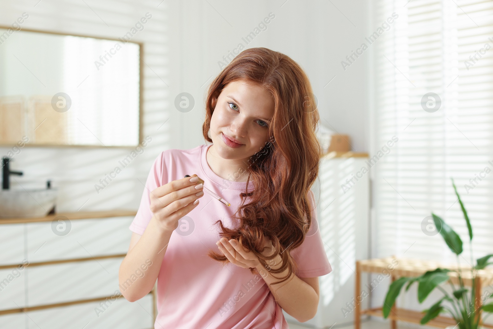 Teenage girl applying cosmetic product onto her hair at home Photo of Teenage girl applying cosmetic product onto her hair at home