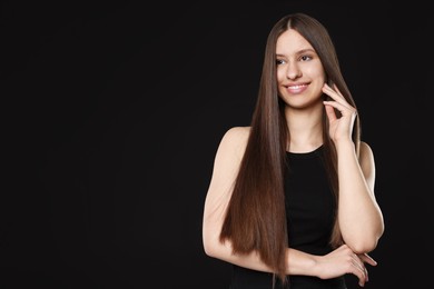 Photo of Smiling teenage girl with healthy long hair on black background. Space for text