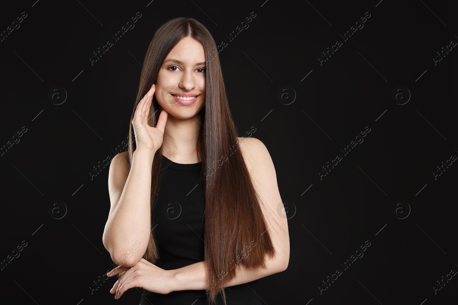 Portrait of smiling teenage girl with healthy long hair on black background Photo of Portrait of smiling teenage girl with healthy long hair on black background