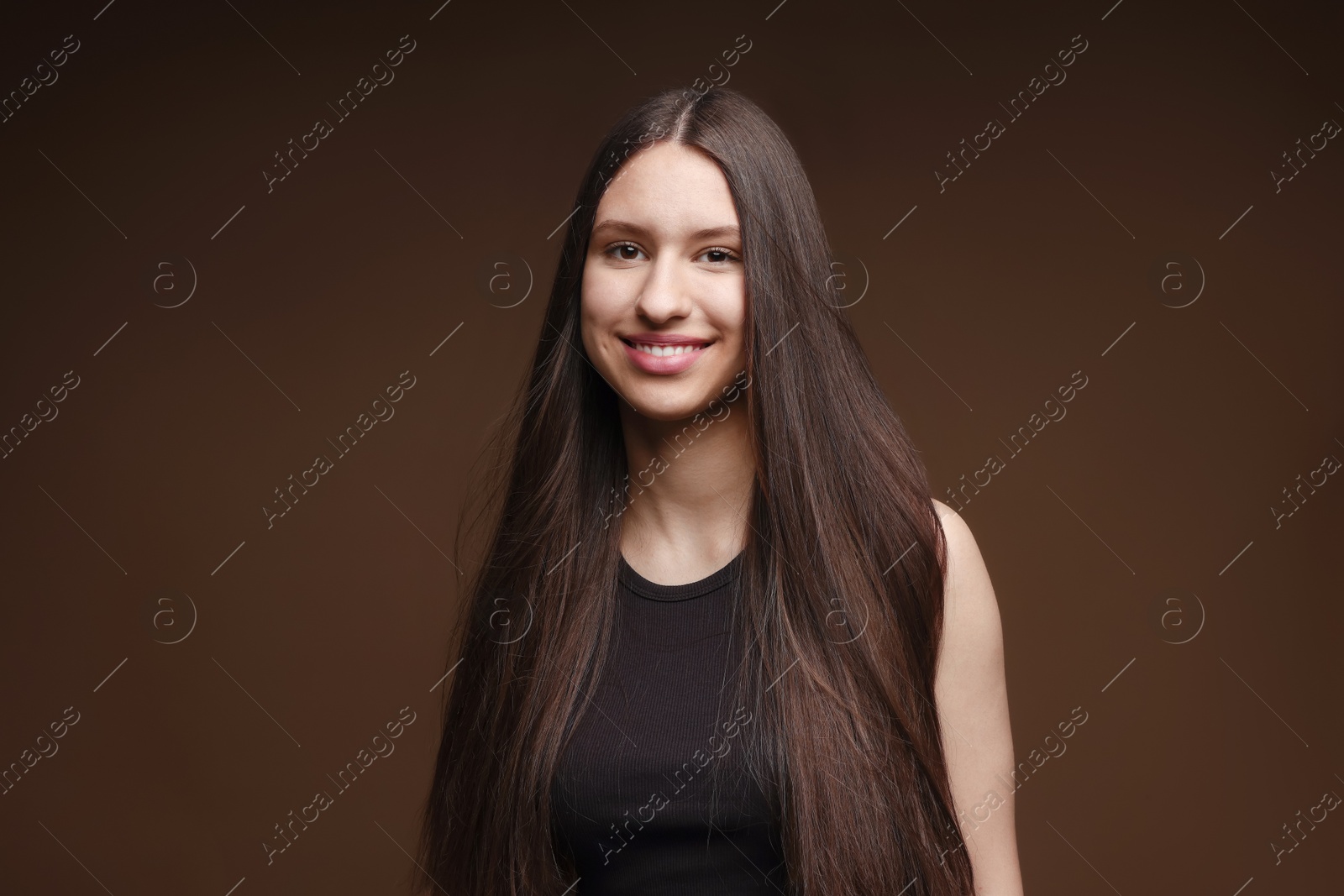 Portrait of smiling teenage girl with healthy long hair on brown background Photo of Portrait of smiling teenage girl with healthy long hair on brown background