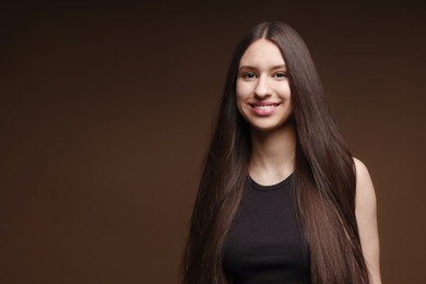Photo of Portrait of smiling teenage girl with healthy long hair on brown background. Space for text