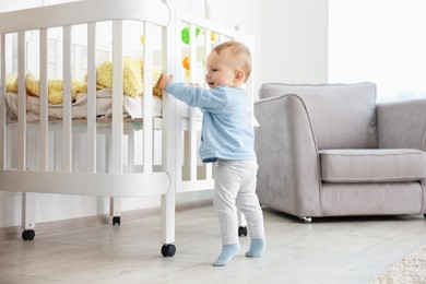 Photo of Cute little baby playing near crib in room