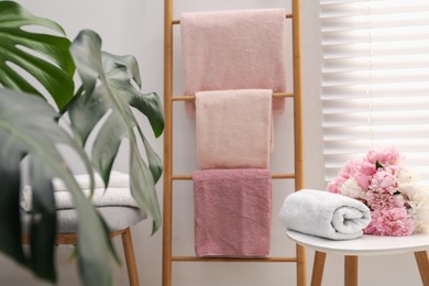 Photo of Soft towels on decorative wooden ladder, peony flowers and green plant in bathroom