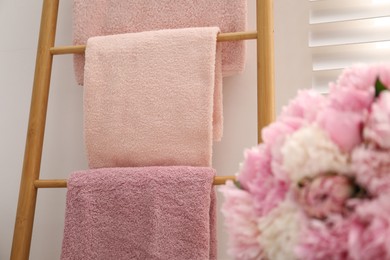 Photo of Soft towels on decorative wooden ladder and peony flowers indoors, closeup