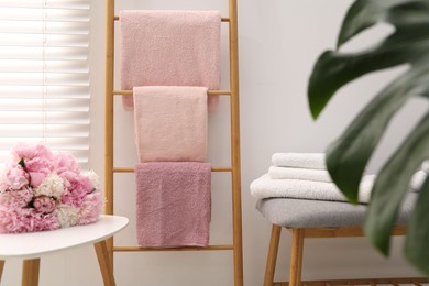 Photo of Soft towels on decorative wooden ladder and peony flowers indoors