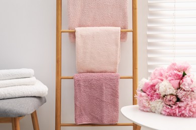 Photo of Soft towels on decorative wooden ladder and peony flowers indoors