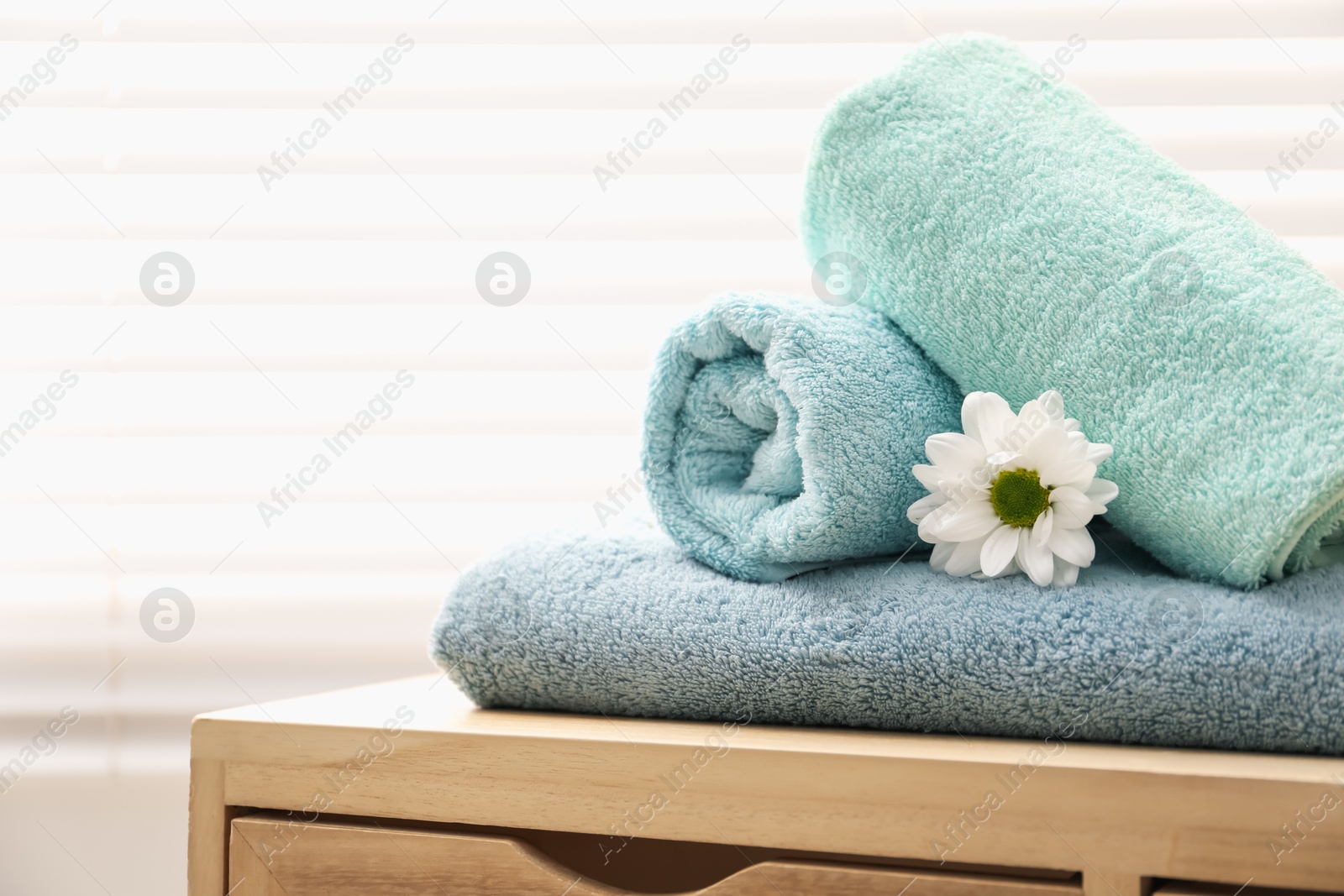 Soft towels and chrysanthemum flower on wooden cabinet indoors, space for text Photo of Soft towels and chrysanthemum flower on wooden cabinet indoors, space for text
