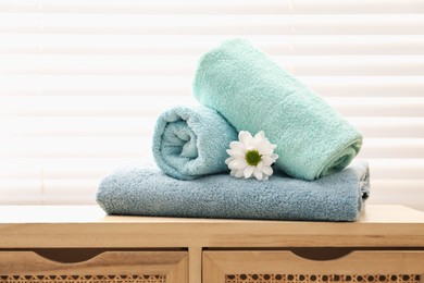 Photo of Soft towels and chrysanthemum flower on wooden cabinet indoors