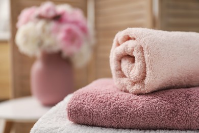 Photo of Stack of soft towels and flowers indoors, closeup. Space for text