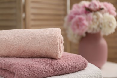 Photo of Stack of soft towels and flowers indoors, closeup. Space for text