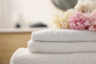 Photo of Stack of soft towels and peony flowers indoors, closeup