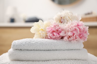 Photo of Stack of soft towels and peony flowers indoors, closeup
