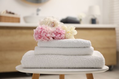 Photo of Stack of soft towels and peony flowers on table in bathroom