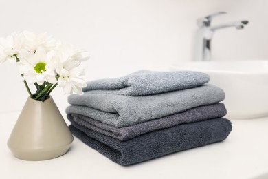 Photo of Stack of soft towels and chrysanthemum flowers on white countertop indoors, closeup