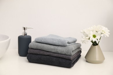 Photo of Stack of soft towels, liquid soap and chrysanthemum flowers on white countertop indoors