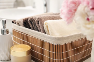 Photo of Soft towels in storage basket, peony flowers and cosmetic products on countertop indoors, closeup
