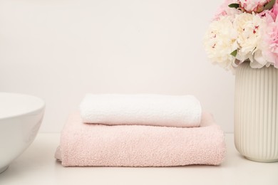 Photo of Soft towels and peony flowers on white countertop indoors, closeup