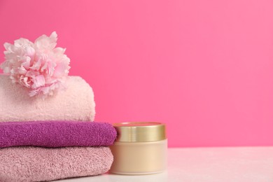 Photo of Soft towels, cosmetic product and peony flower on table against pink background, closeup. Space for text
