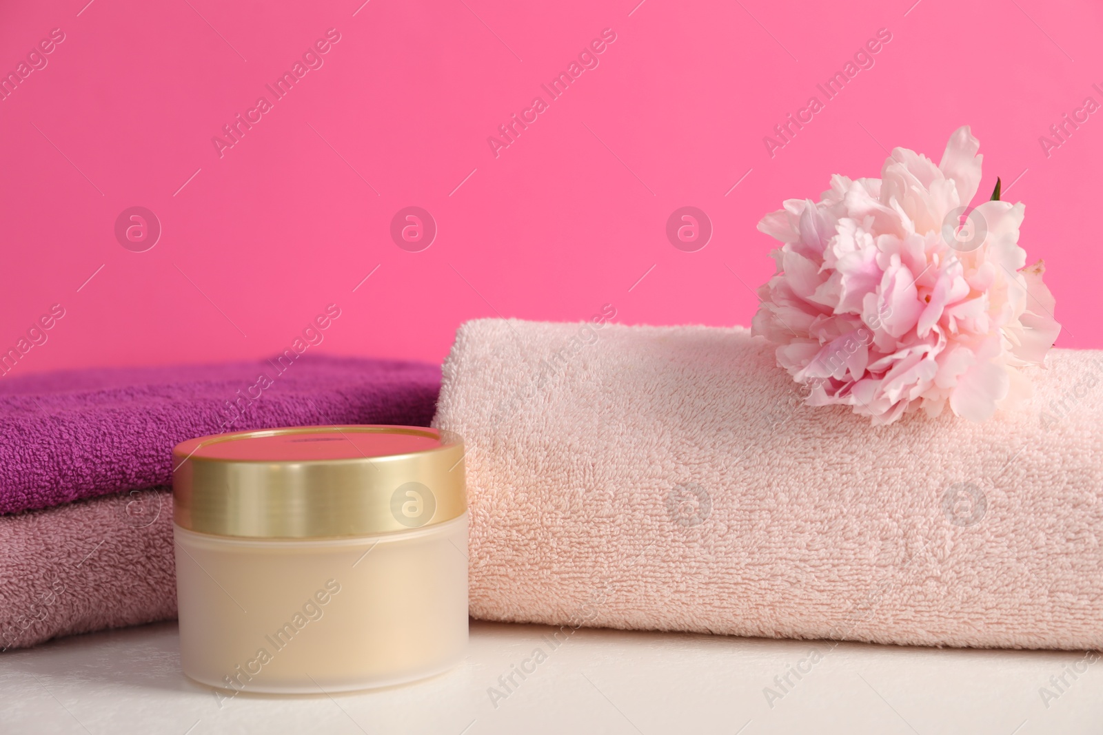 Soft towels, cosmetic product and peony flower on white table against pink background, closeup Photo of Soft towels, cosmetic product and peony flower on white table against pink background, closeup