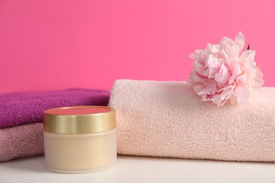 Photo of Soft towels, cosmetic product and peony flower on white table against pink background, closeup