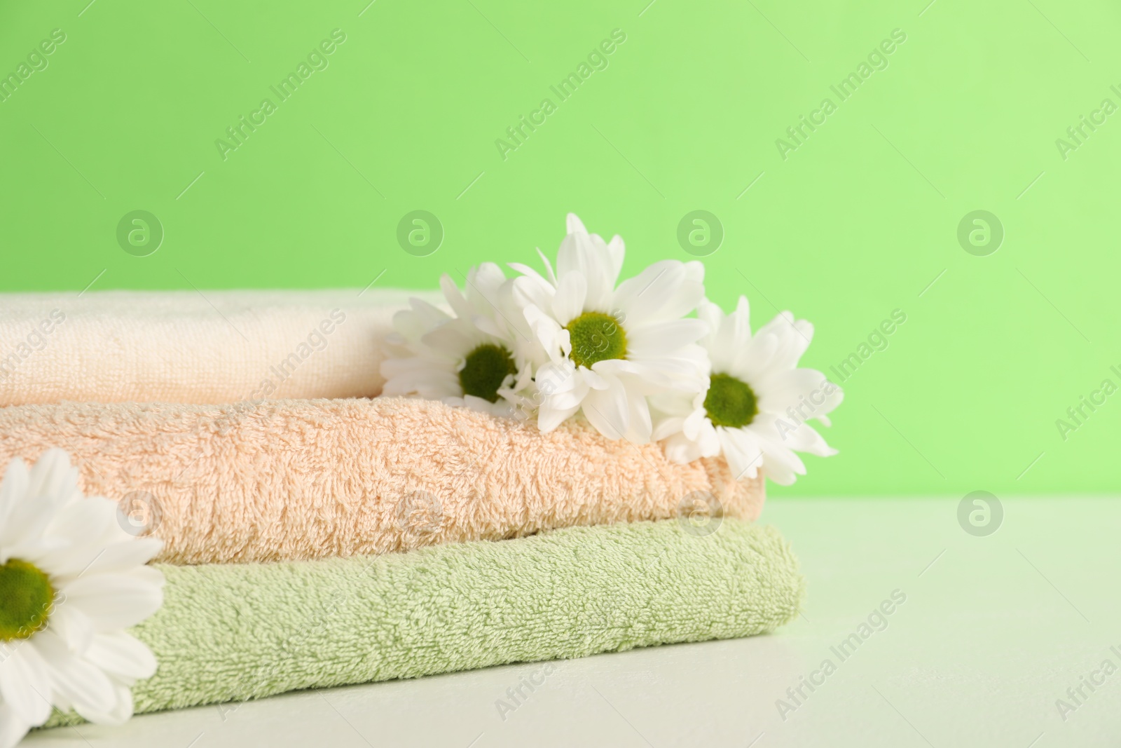 Soft towels and chrysanthemum flowers on green background, closeup. Space for text Photo of Soft towels and chrysanthemum flowers on green background, closeup. Space for text