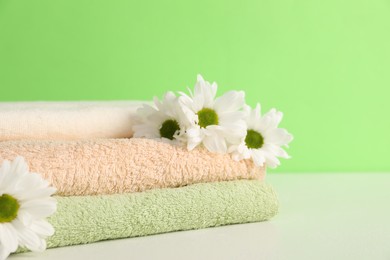 Photo of Soft towels and chrysanthemum flowers on green background, closeup. Space for text