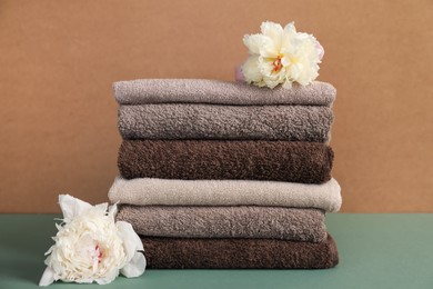 Photo of Stack of soft towels and peony flowers on color background