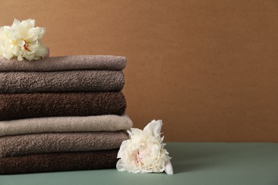 Photo of Stack of soft towels and peony flowers on color background, closeup. Space for text