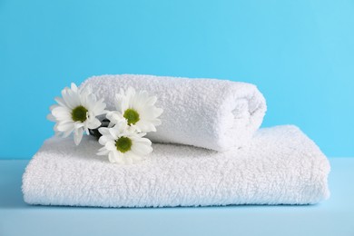 Photo of Soft towels and chrysanthemum flowers on light blue background