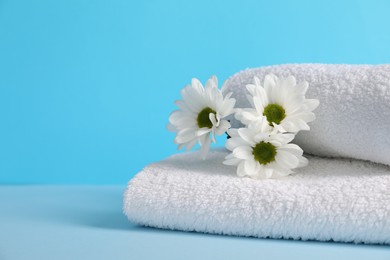 Photo of Soft towels and chrysanthemum flowers on light blue background, closeup. Space for text
