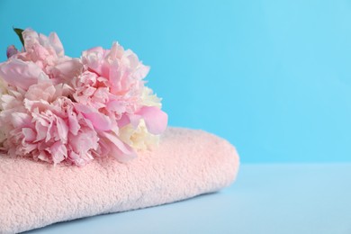 Photo of Soft towel and peony flowers on light blue background, closeup. Space for text