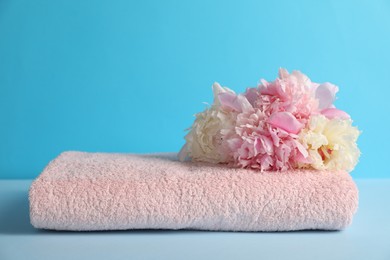 Photo of Soft towel and peony flowers on light blue background, closeup