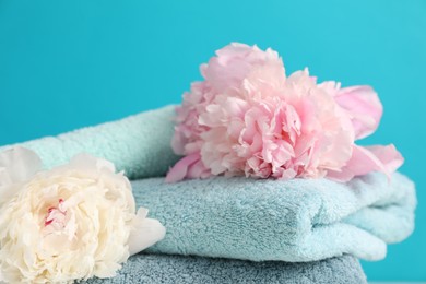 Photo of Soft towels and peony flowers on light blue background, closeup