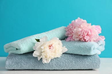 Photo of Soft towels and peony flowers on white table against light blue background, closeup