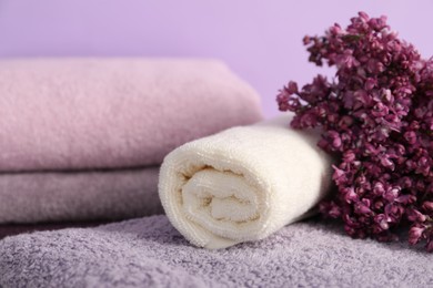 Photo of Soft towels and lilac flowers on violet background, closeup