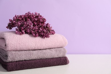 Photo of Soft towels and lilac flowers on white table against violet background, closeup. Space for text