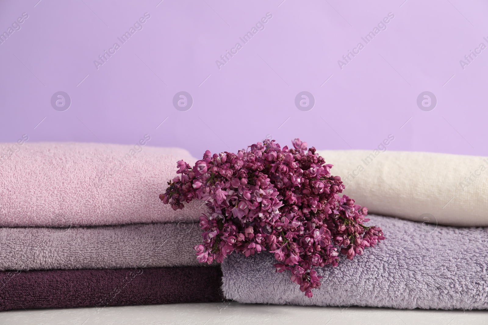 Soft towels and lilac flowers on white table against violet background, closeup Photo of Soft towels and lilac flowers on white table against violet background, closeup