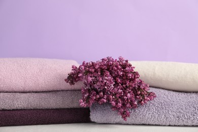 Photo of Soft towels and lilac flowers on white table against violet background, closeup