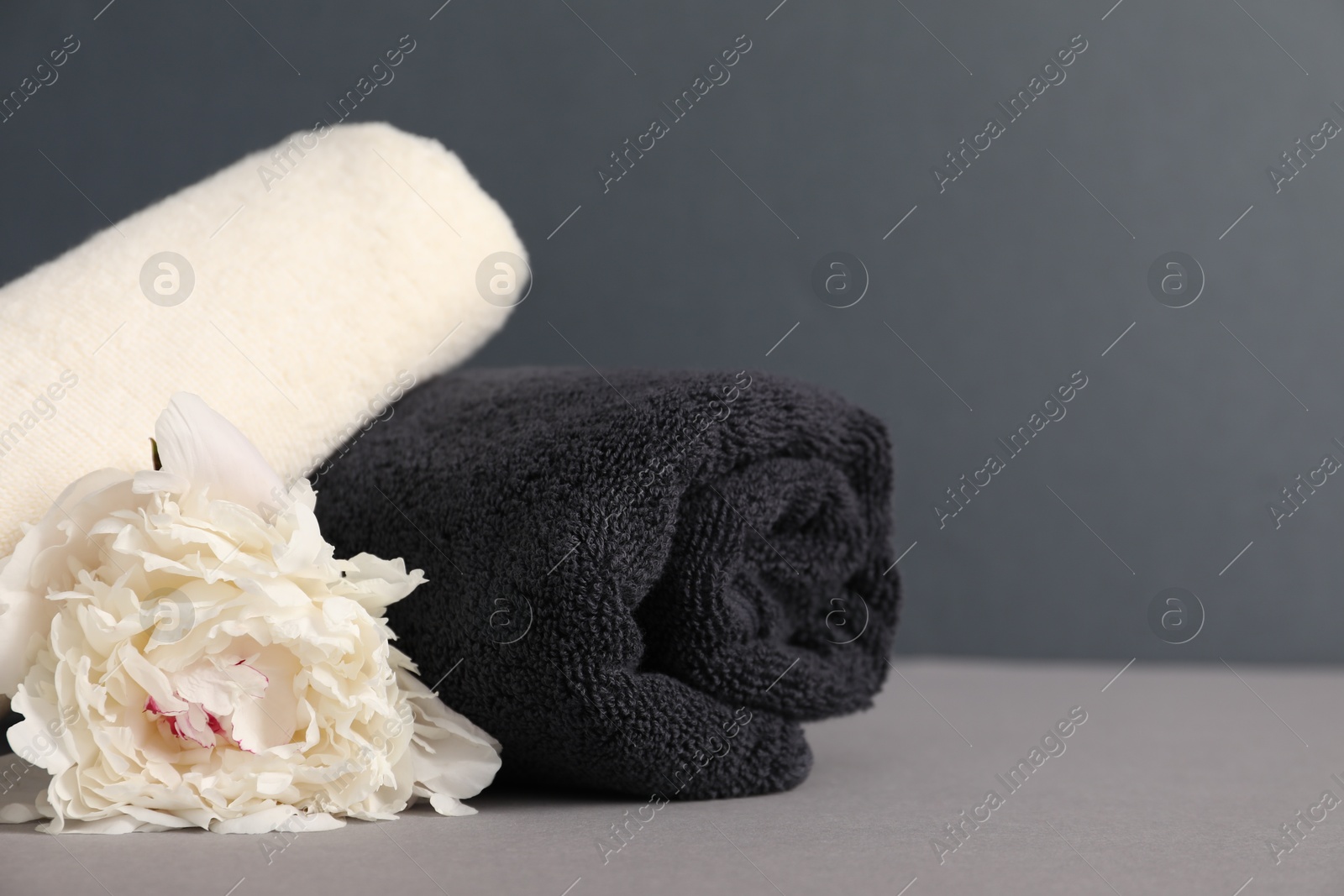 Soft towels and peony flower on grey background, closeup. Space for text Photo of Soft towels and peony flower on grey background, closeup. Space for text