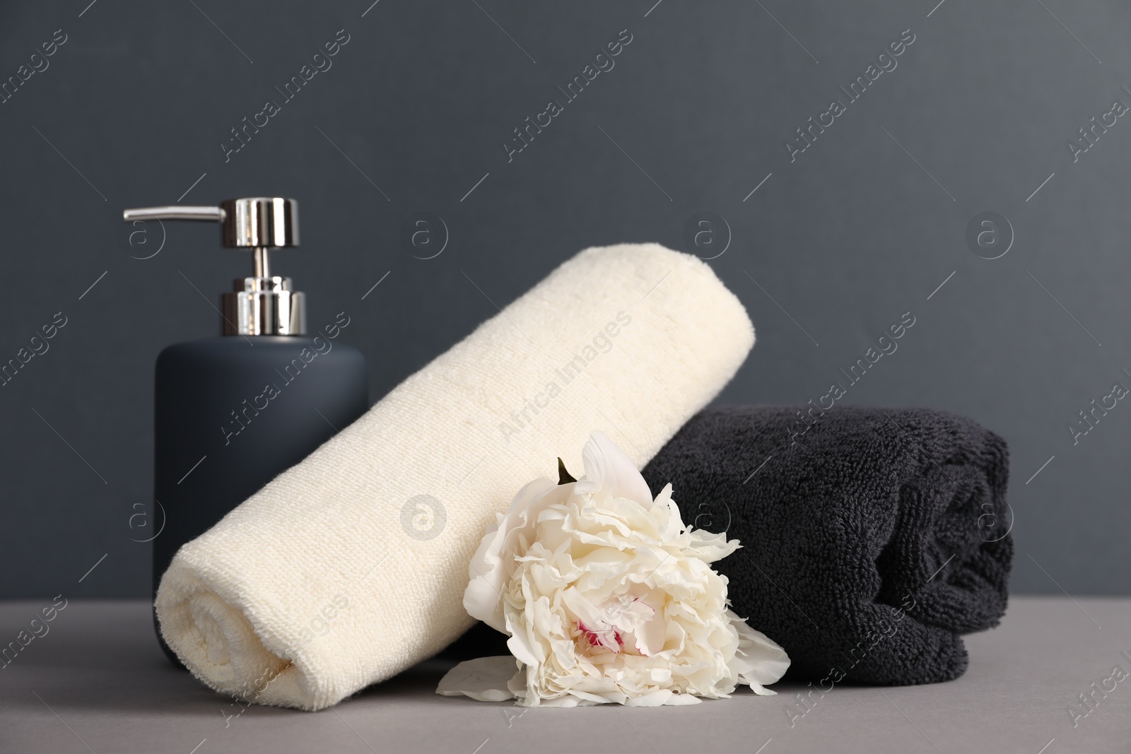 Soft towels, peony flower and liquid soap on grey background Photo of Soft towels, peony flower and liquid soap on grey background