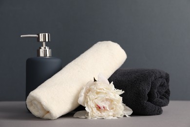 Photo of Soft towels, peony flower and liquid soap on grey background