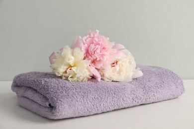 Photo of Soft towel and peony flowers on light grey background, closeup