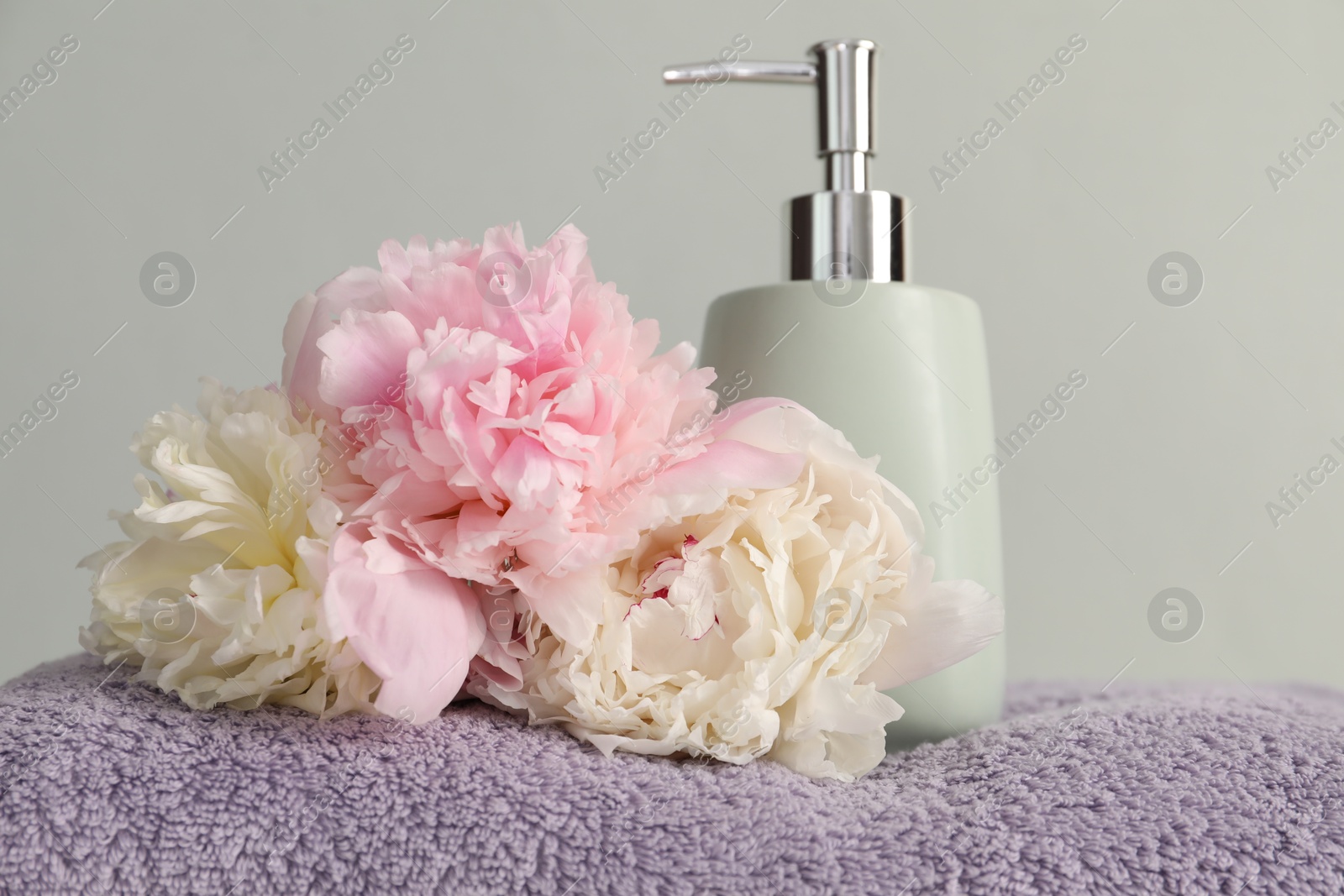 Soft towel, peony flowers and liquid soap on light grey background, closeup Photo of Soft towel, peony flowers and liquid soap on light grey background, closeup