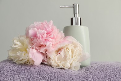 Photo of Soft towel, peony flowers and liquid soap on light grey background, closeup