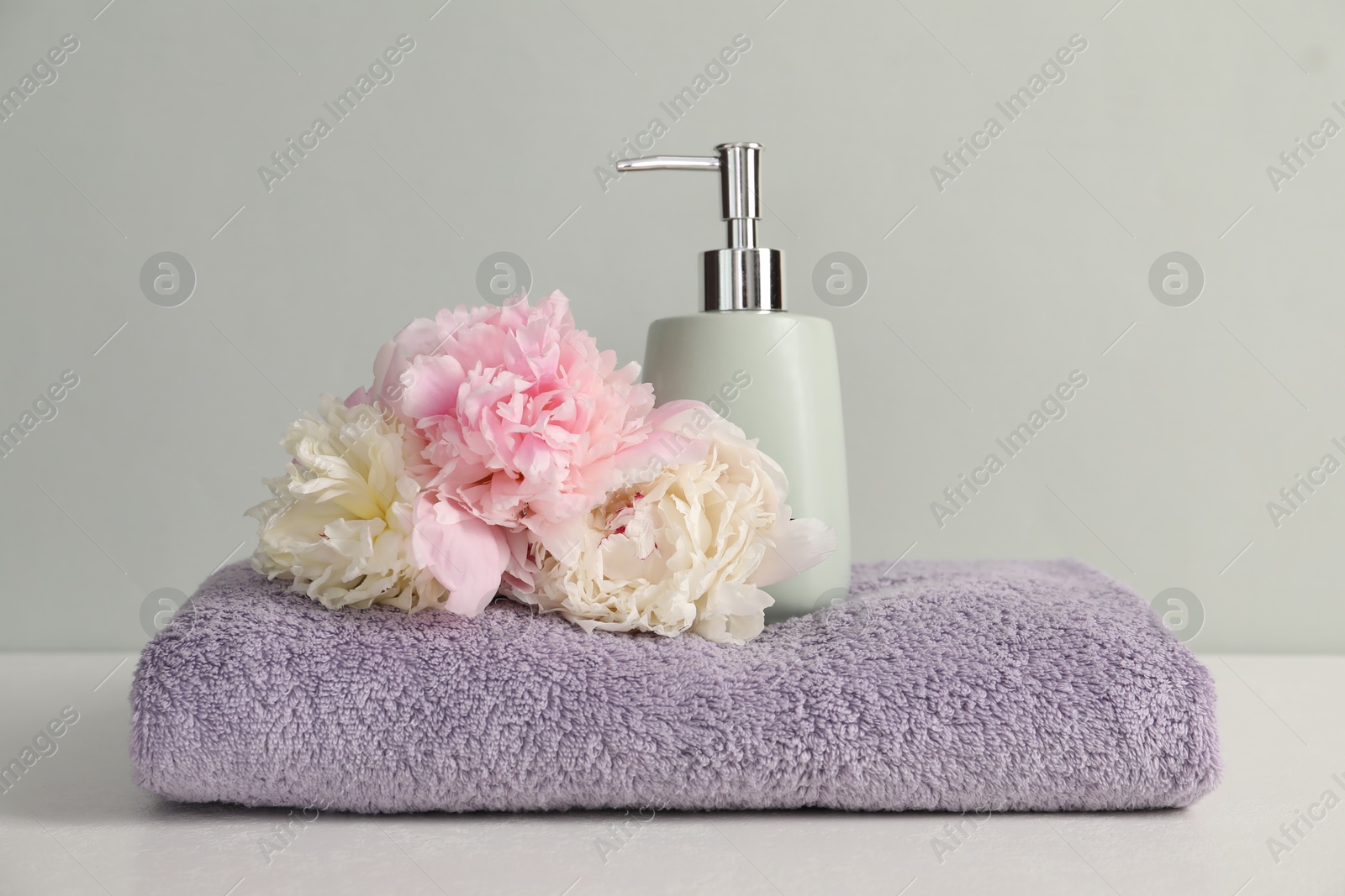 Soft towel, peony flowers and liquid soap on light grey background Photo of Soft towel, peony flowers and liquid soap on light grey background
