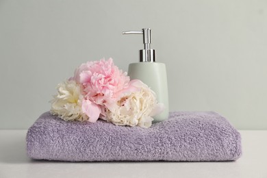 Photo of Soft towel, peony flowers and liquid soap on light grey background